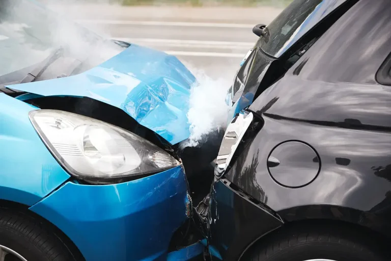 Close-up of a front-end collision between a blue car and a black car with smoke rising from the crumpled hood, ideal for personal injury claims and car accident insurance content.