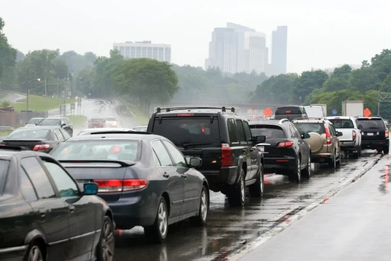 Heavy traffic congestion on a wet highway during a rainy day with a city skyline in the background, illustrating hazardous driving conditions and car accident risks.