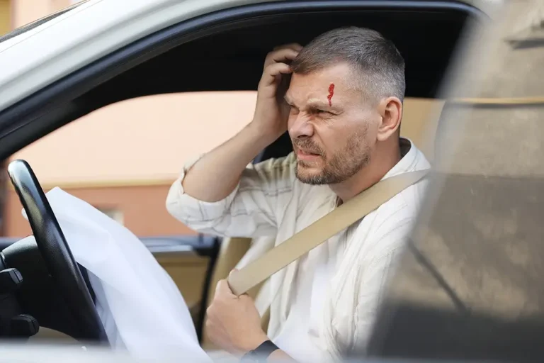 Injured male driver with a bleeding head wound sitting in a car after a crash with a deployed airbag.