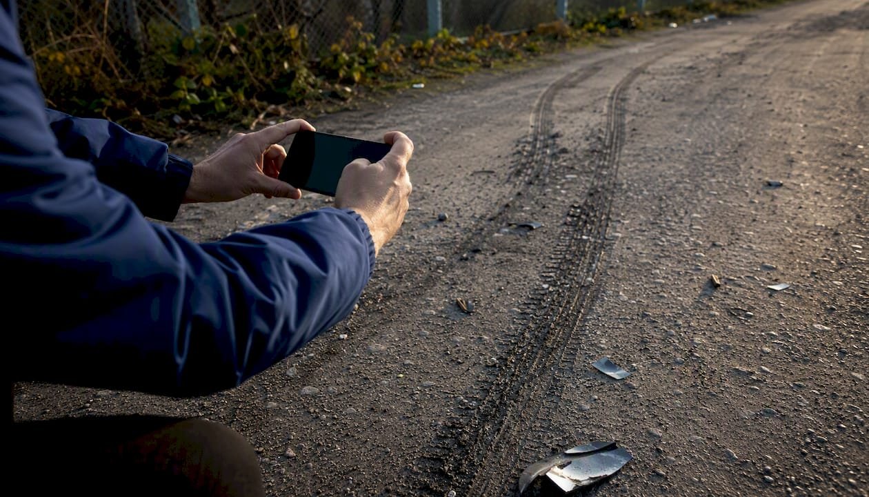 Hands photographing skid marks with phone